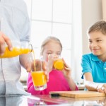 Midsection of father serving orange juice for children in kitchen